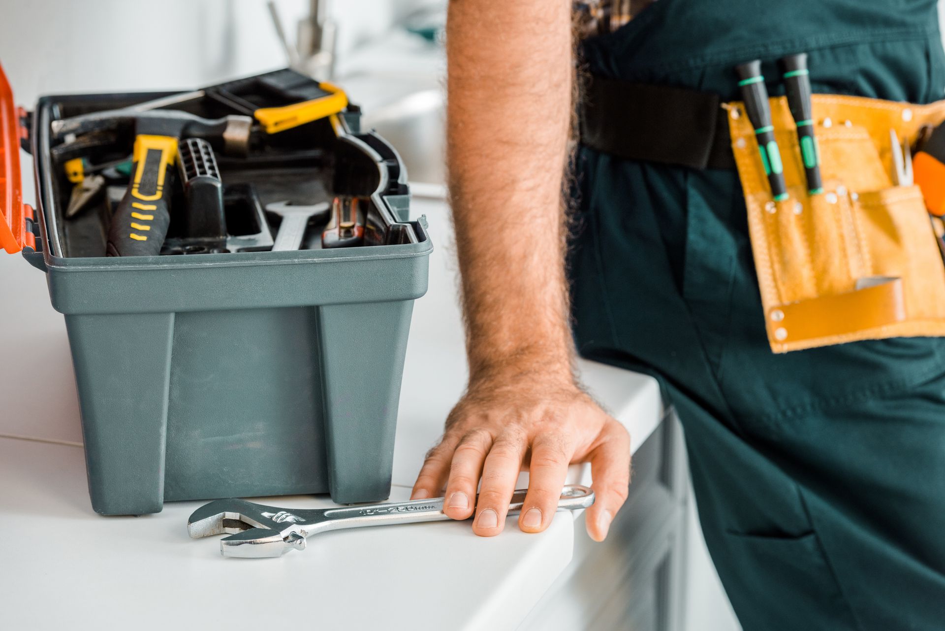 Cropped image of plumber leaning on kitchen counter and touching adjustable wrench in kitchen