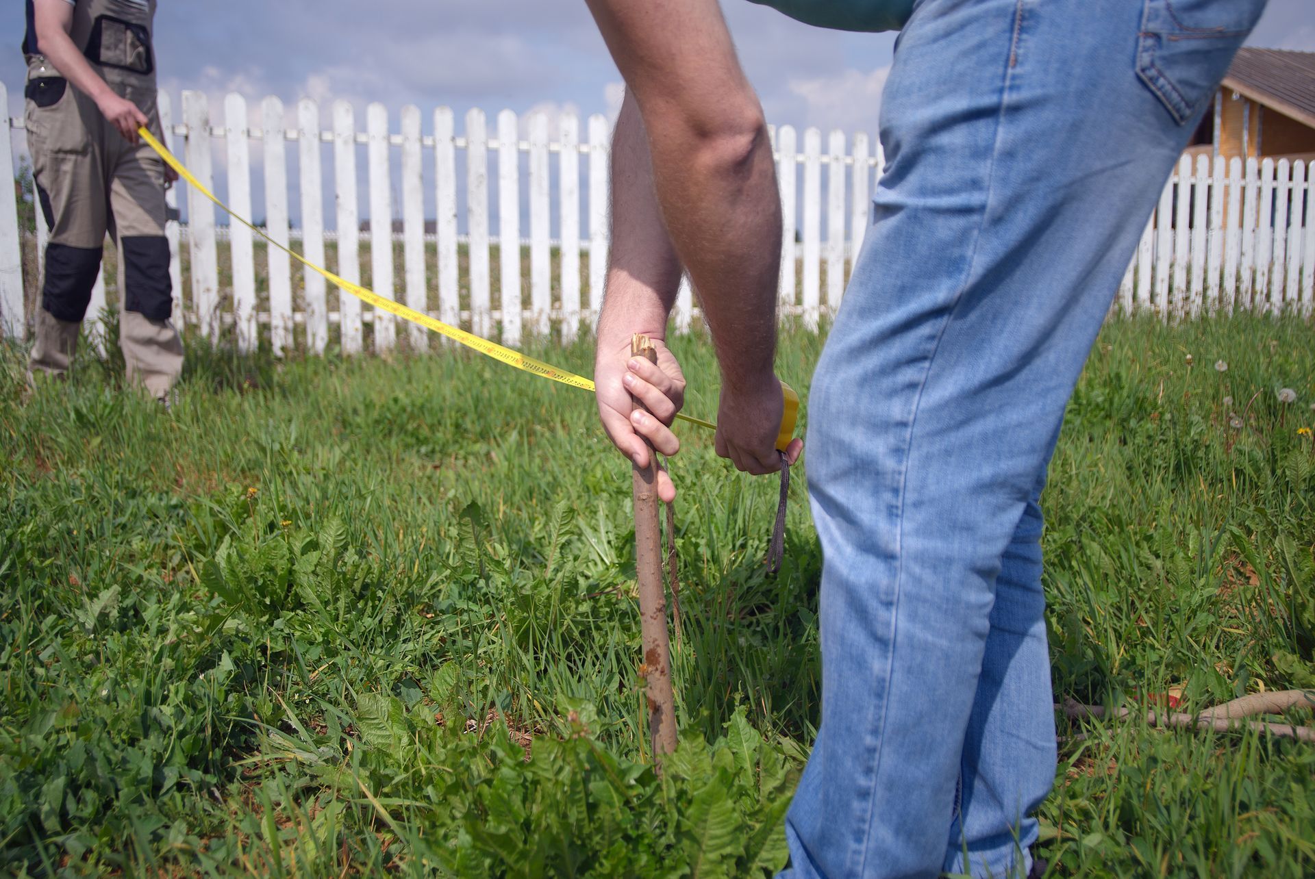 A man is measuring a pole in the grass with a tape measure.