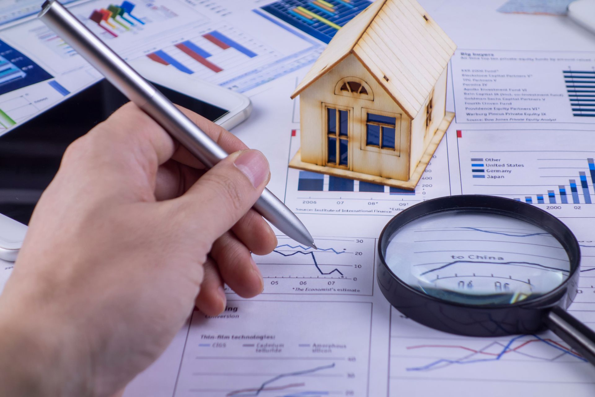 A person is writing on a piece of paper next to a magnifying glass and a model house.