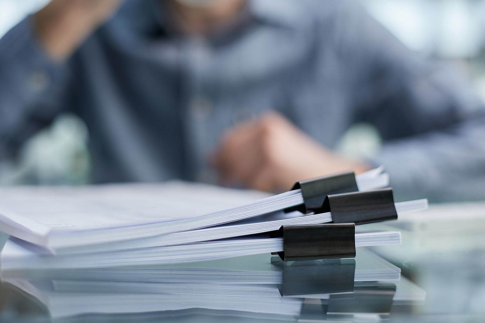 A man is sitting at a desk with a stack of papers on it.