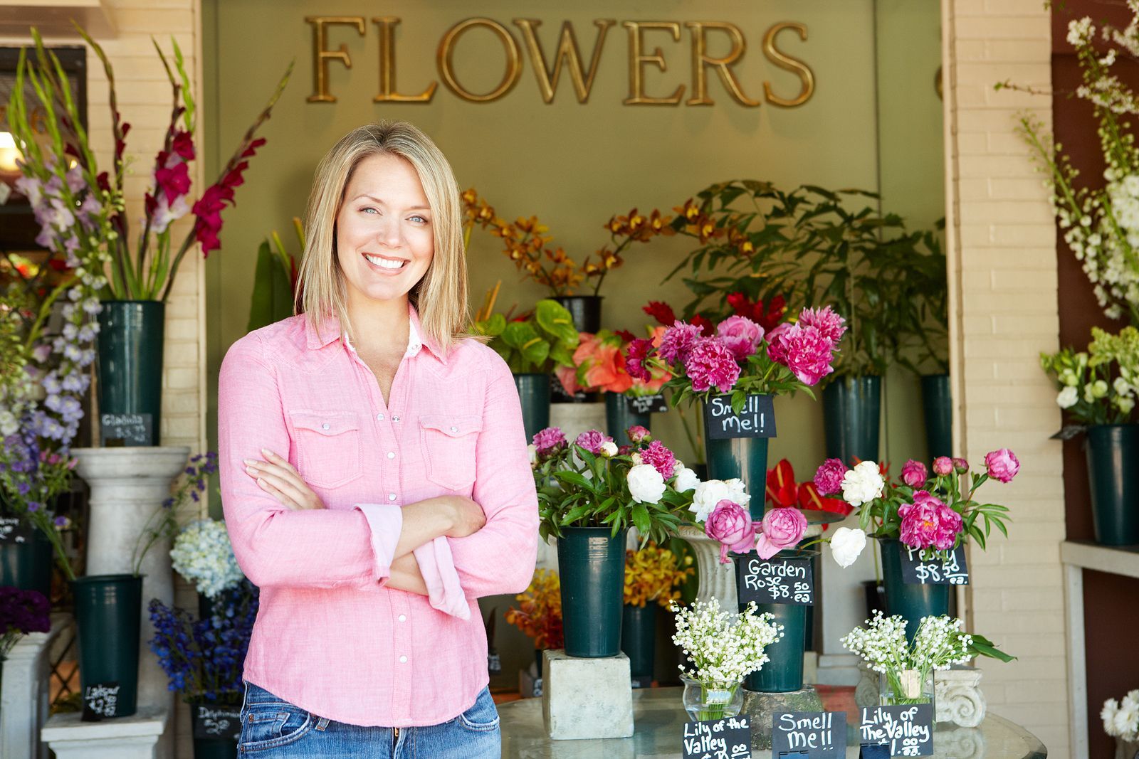 Small Business owner in pink shirt standing in front of flower shop display with colorful bouquets