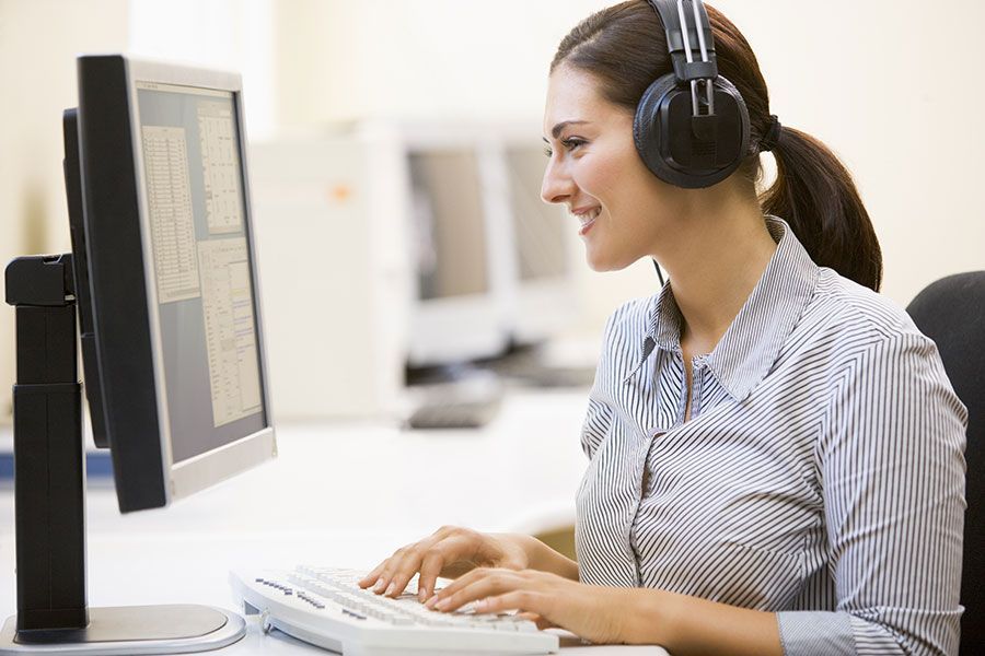 A woman wearing headphones is typing on a computer keyboard.