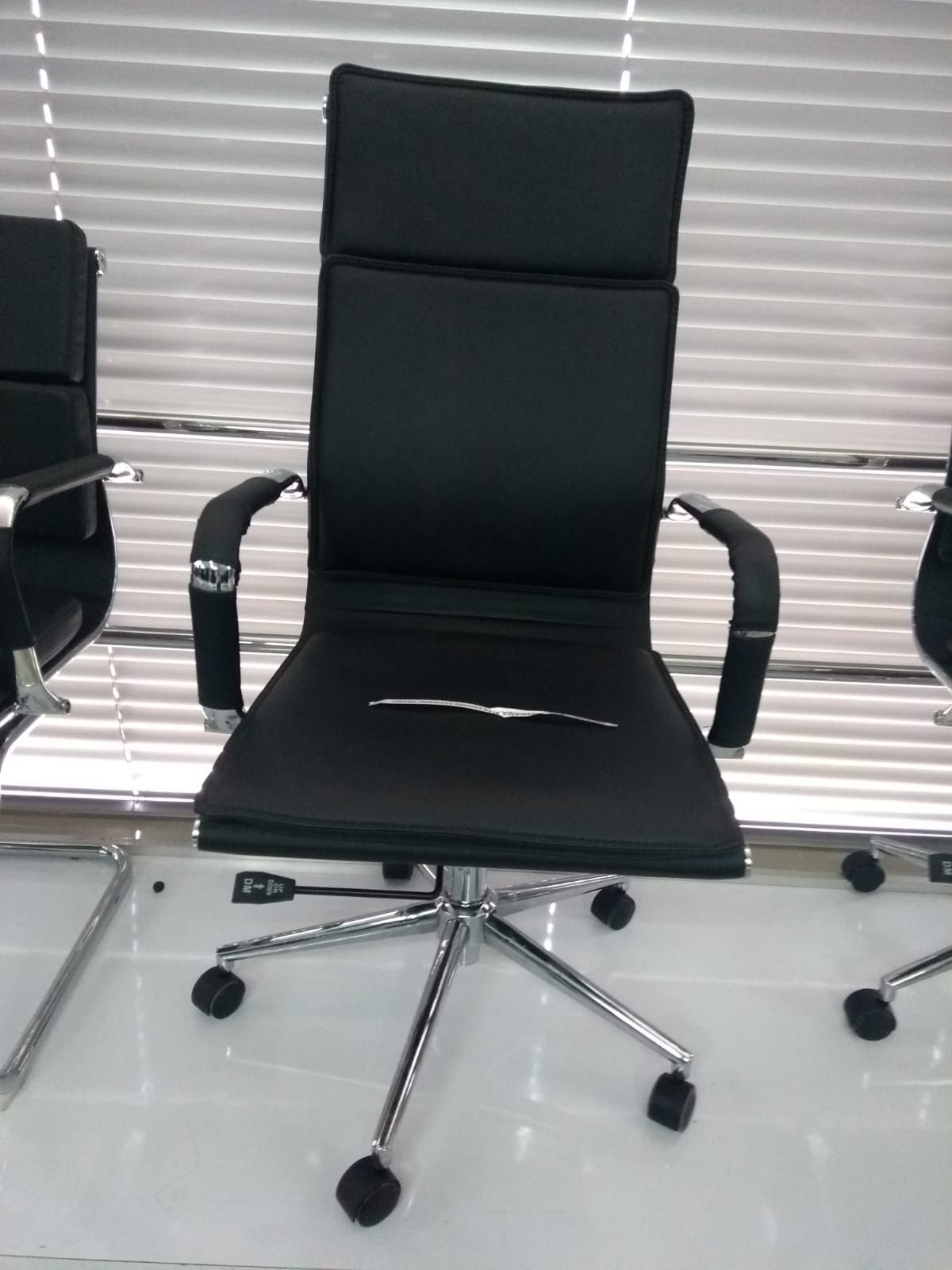 Silla de oficina negra con reposabrazos y base cromada frente a las persianas.