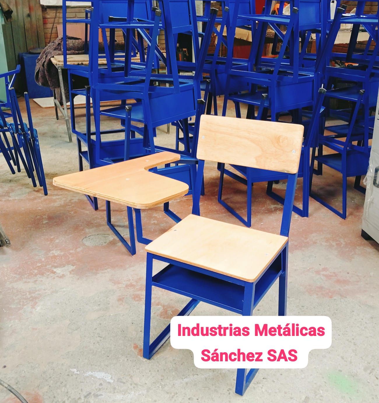 Pupitres escolares de metal azul con tableros de madera clara apilados en un taller