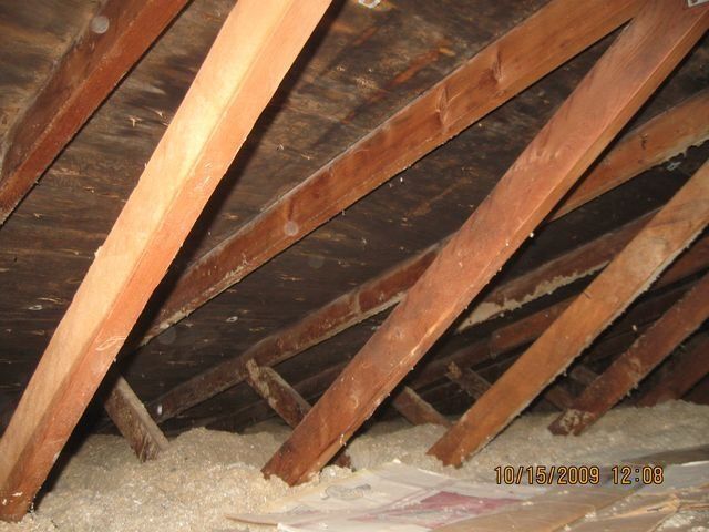 Attic with exposed wooden rafters and insulation piled along the floor.