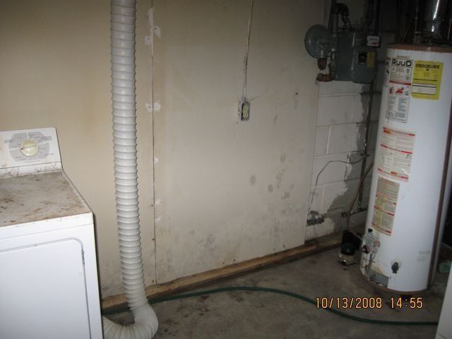 Mold-covered room with peeling ceiling, damaged walls, and an open door under a bare lightbulb.