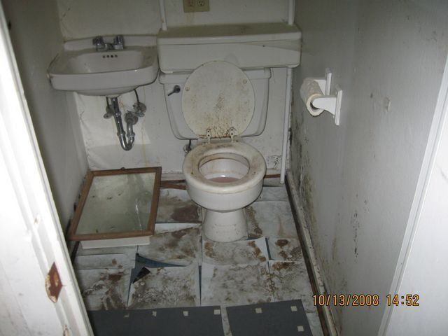 Damaged ceiling panel with stains and a small exposed pipe in a white room