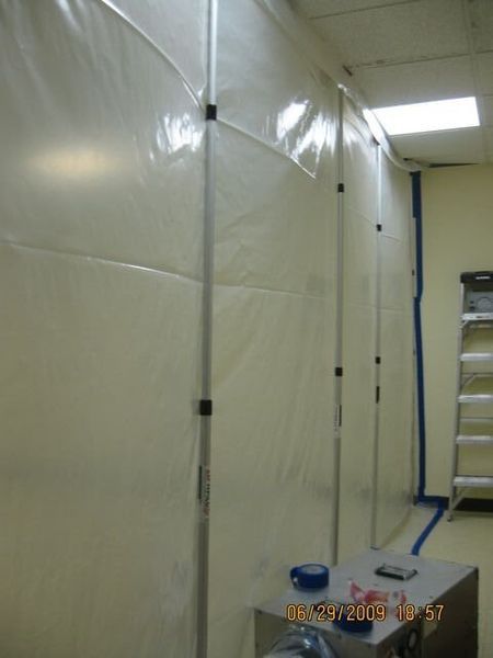 Plastic-covered corridor with a small ladder and blue tape on the floor under fluorescent lights