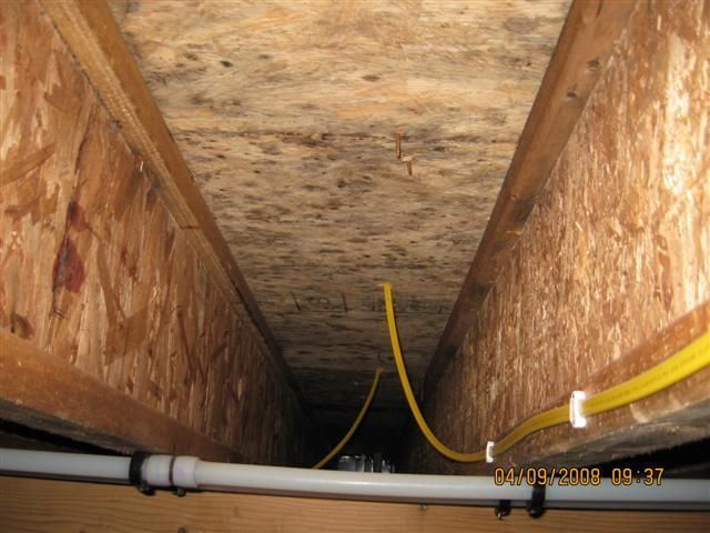 Attic crawlspace with exposed wooden rafters, insulation, and yellow electrical conduit running along the floor.