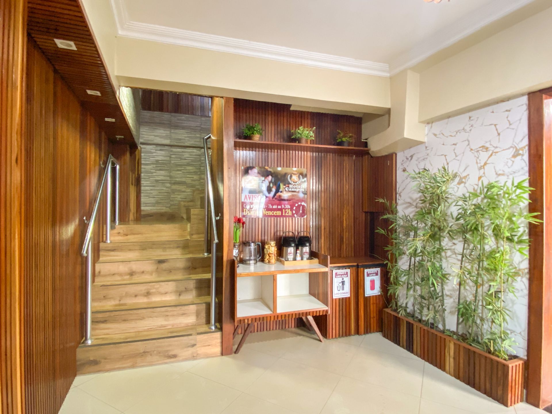 Hall de entrada com painéis de madeira, escadas, prateleiras na parede e vasos de bambu.