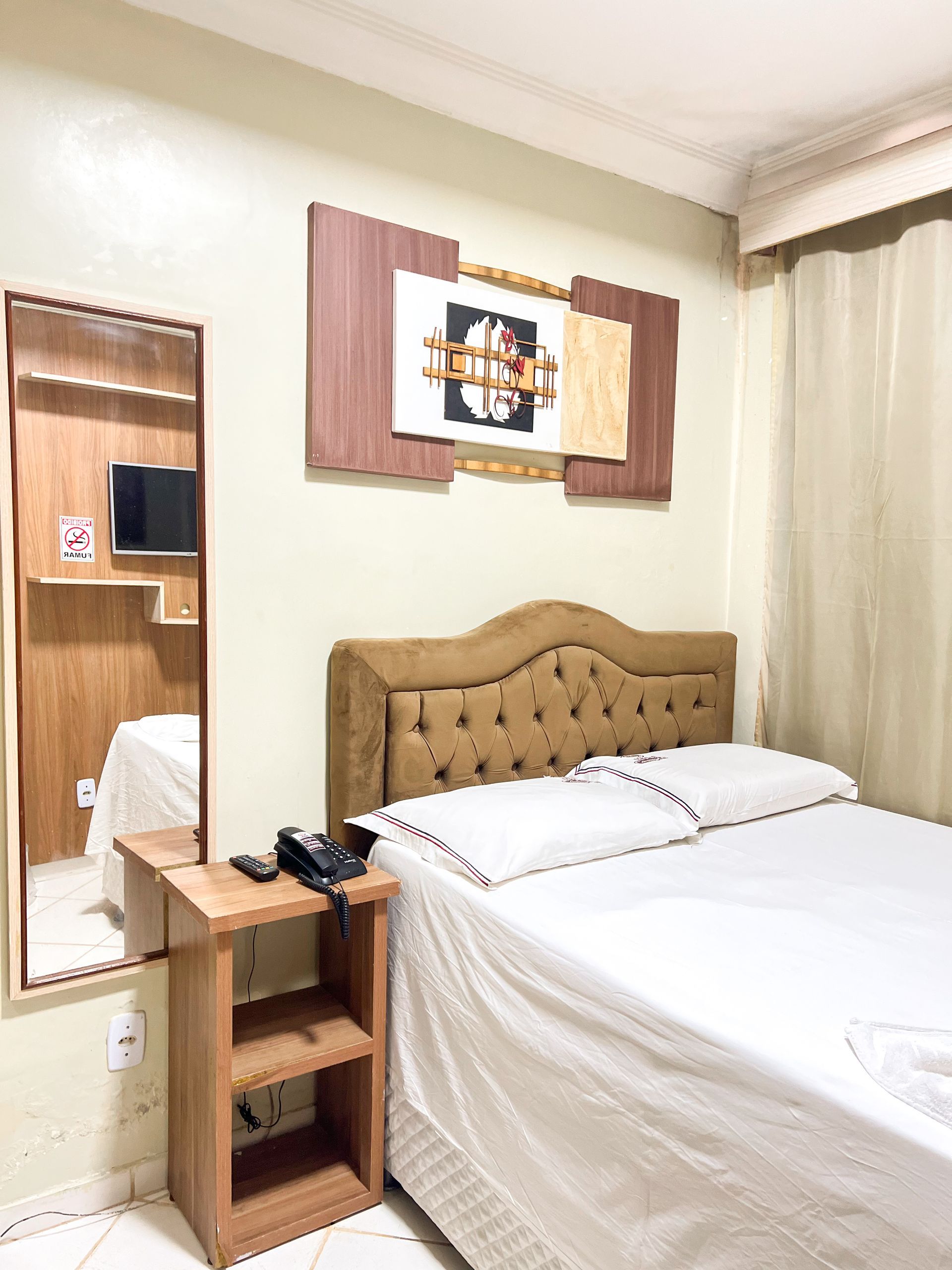 Quarto aconchegante com roupa de cama branca, cabeceira estofada, mesa de cabeceira e espelho de parede em um ambiente bege suave.
