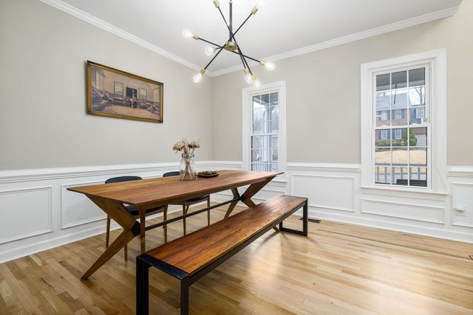 Dining room with wooden table and bench, white wainscoting, hardwood floor, and large windows