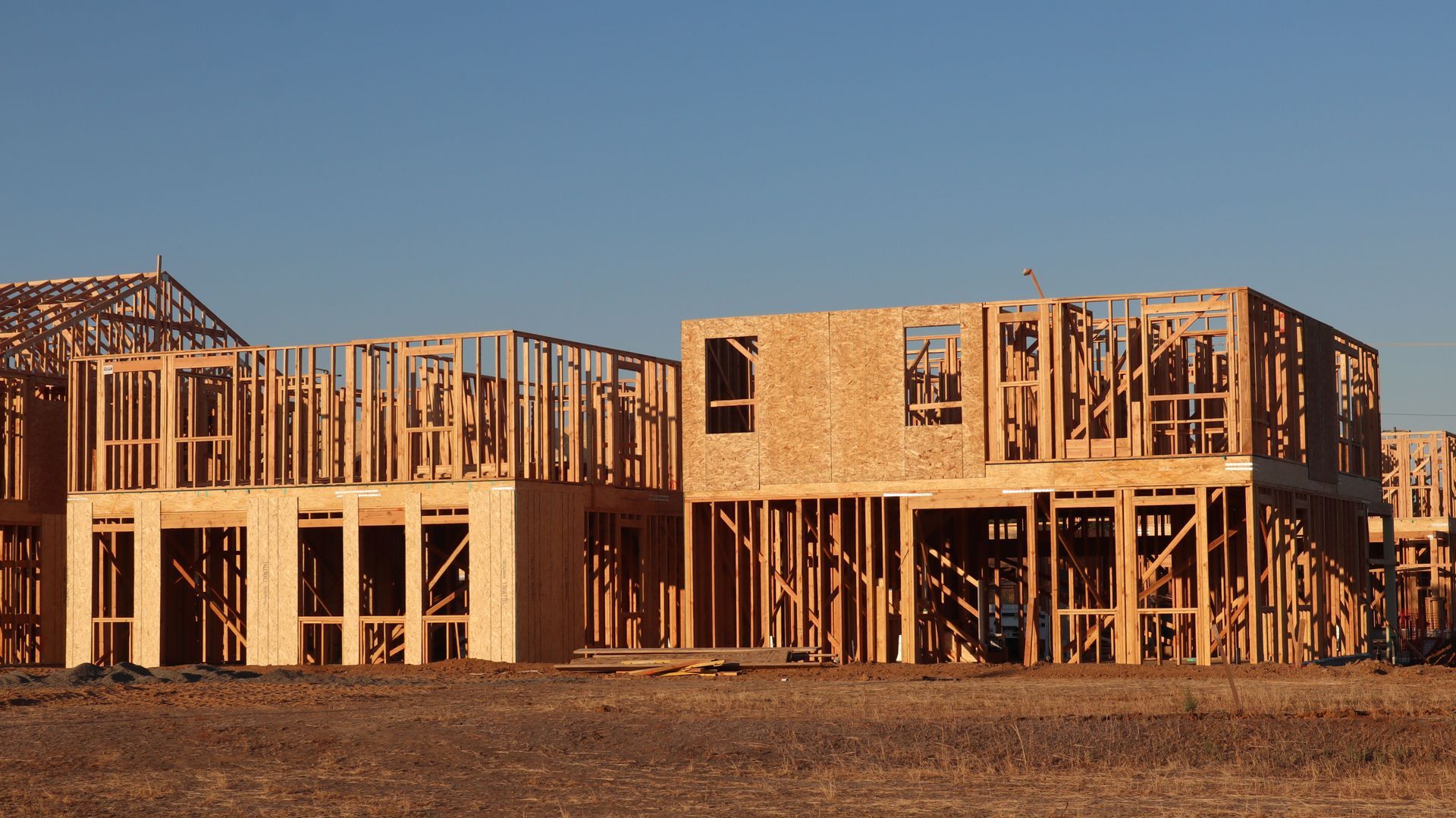 Wood-framed house under construction in a barren lot at sunset