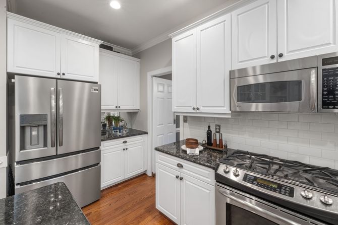 Modern kitchen with white cabinets, stainless steel appliances, and a gas range on wood floors