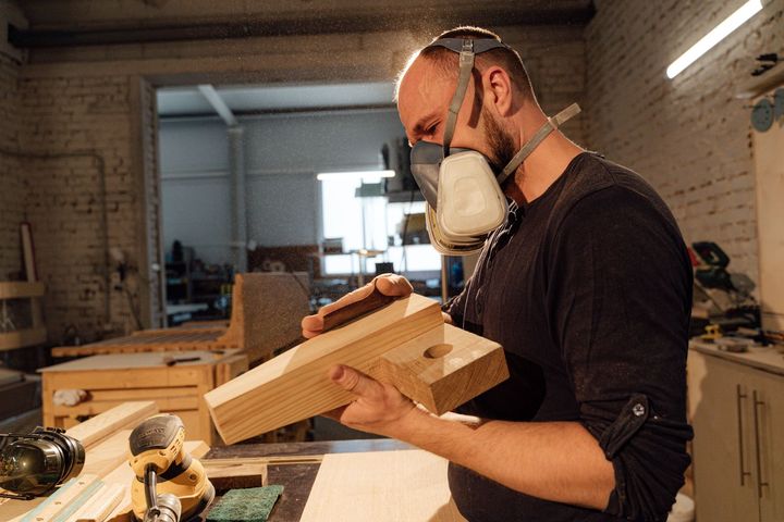 Woodworker in a dust mask shaping a wooden board in a workshop