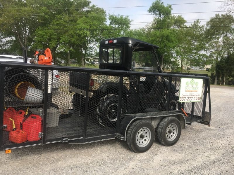 A black UTV parked on a utility trailer, with red fuel cans and equipment stored in the front area.
