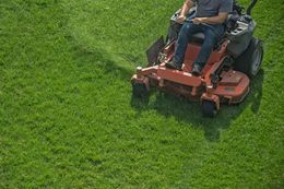 A person rides a bright orange zero-turn lawn mower across a vibrant green lawn.
