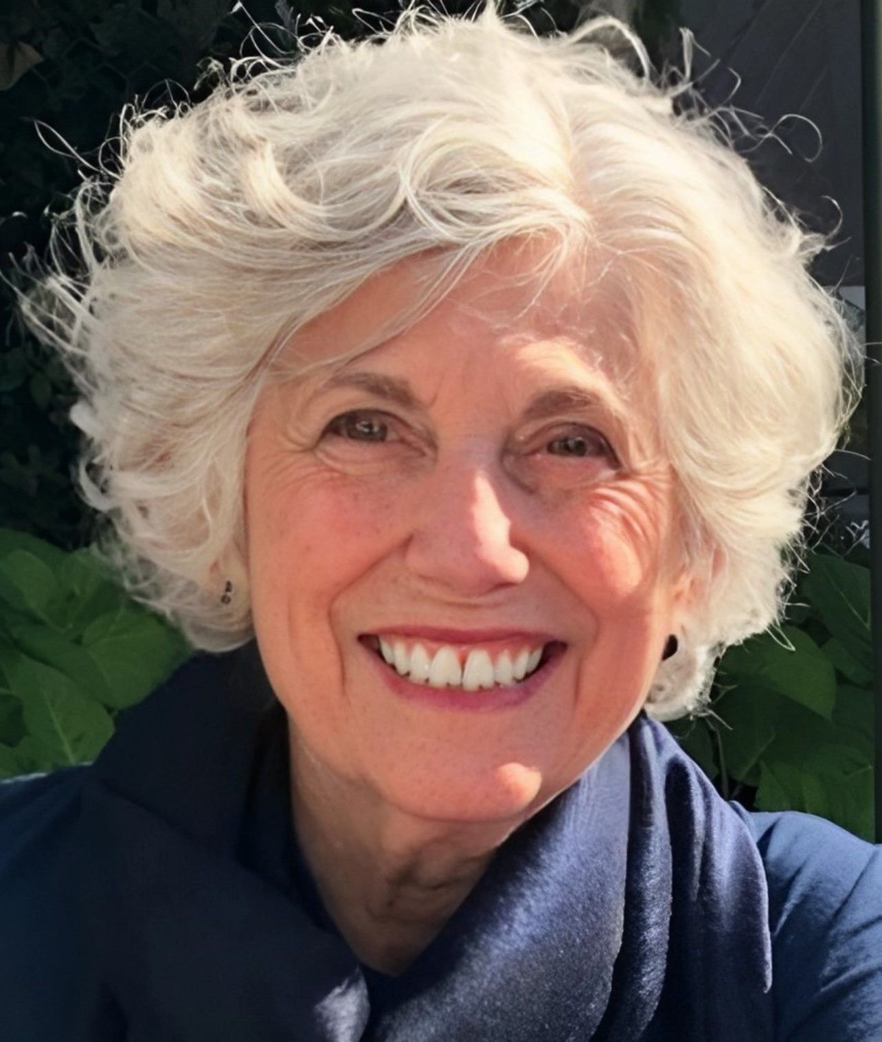Smiling woman with short white hair, outdoors in a navy scarf.