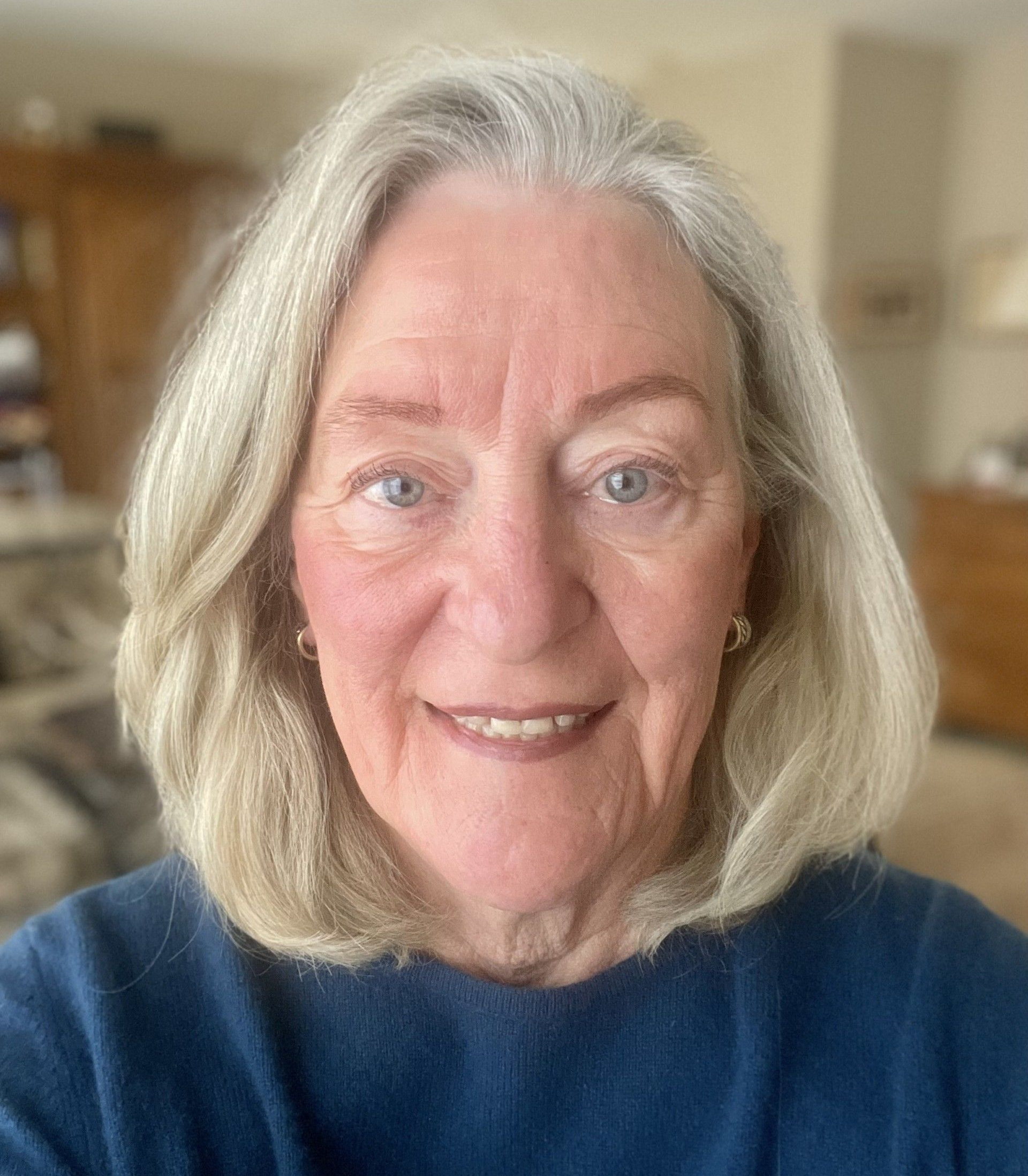 Smiling woman with shoulder-length gray hair wearing a blue sweater indoors