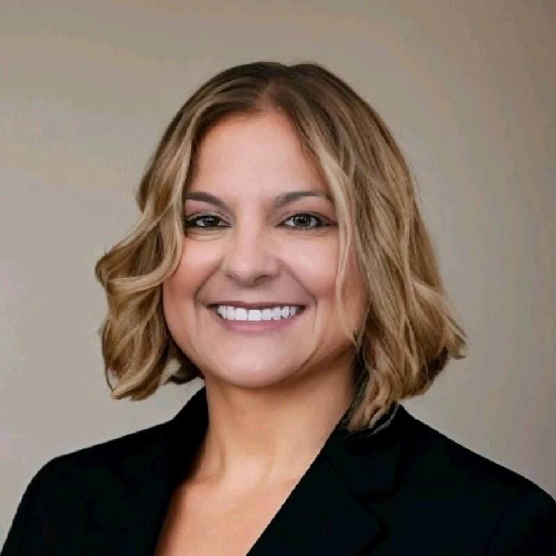 Smiling person in a black blazer against a neutral background