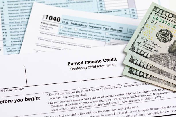 Tax forms, Earned Income Credit information, and US currency arranged on a desk.