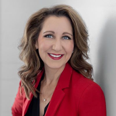 Woman in a red blazer smiling against a light gray background