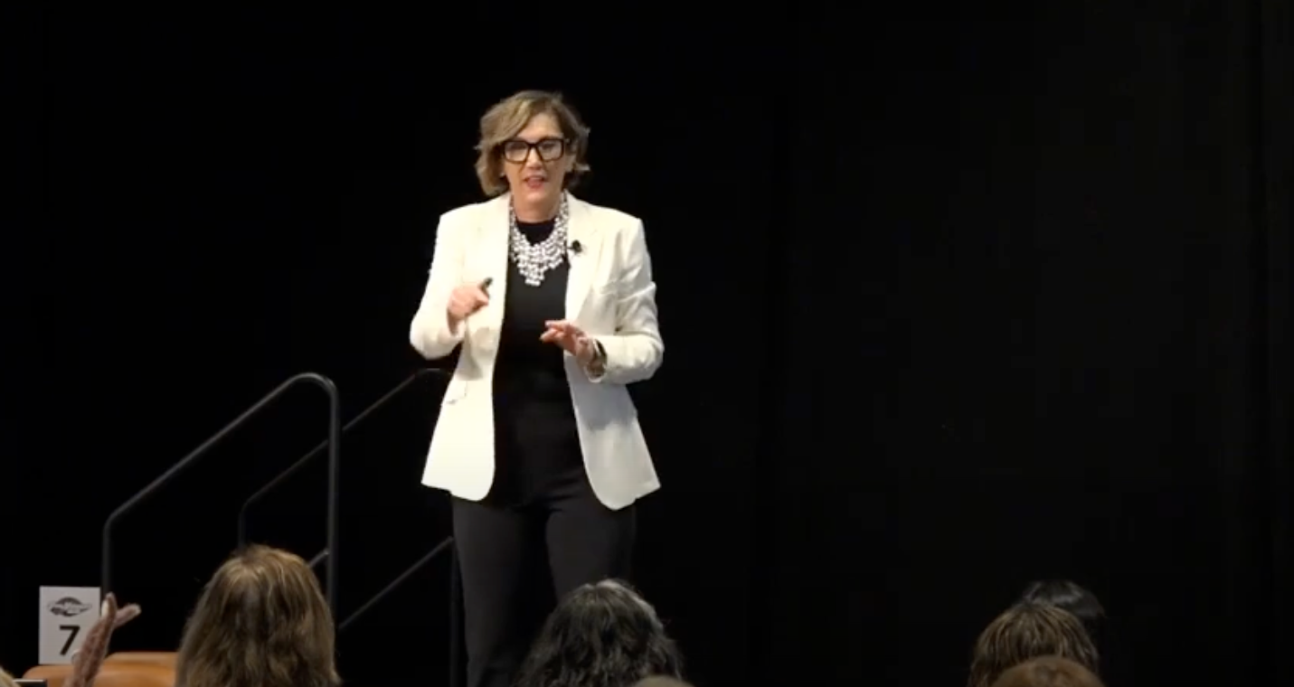 A woman is standing on a stage giving a presentation to a group of people.