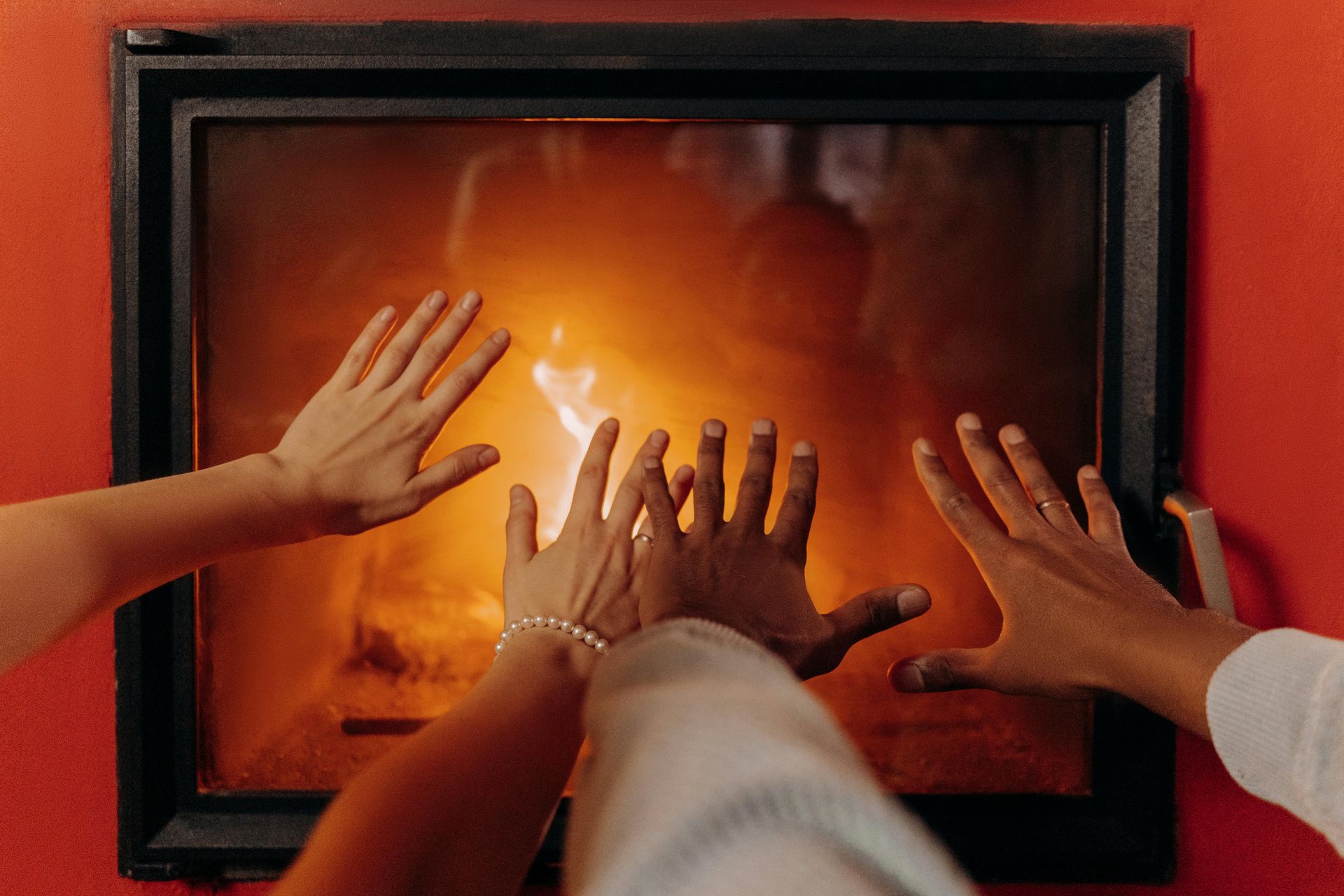 Three hands pressed toward a glowing fire behind a glass window in a black frame
