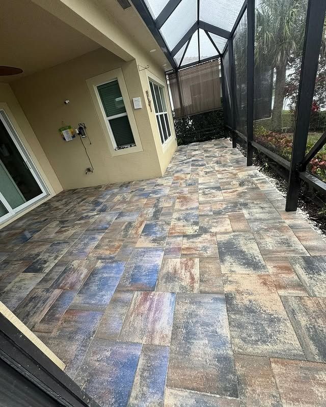 A patio with rectangular multi-colored stone pavers under a screened enclosure attached to a house.