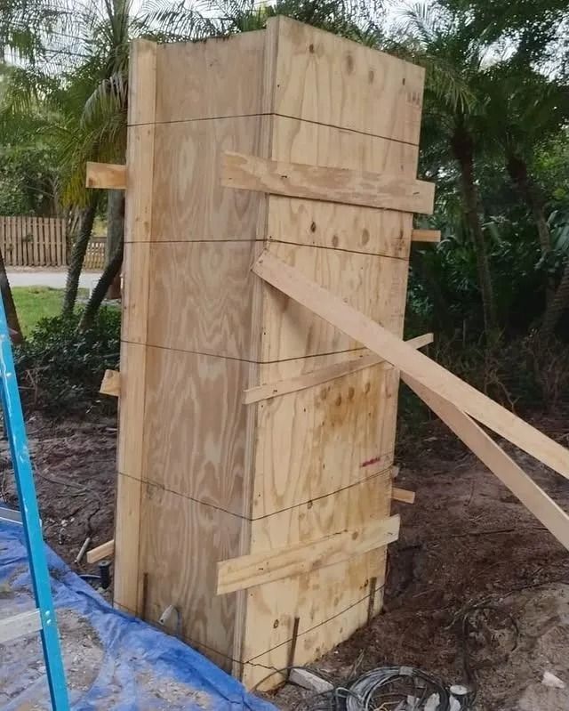 A rectangular plywood form for a concrete column stands braced in an outdoor, grassy area.