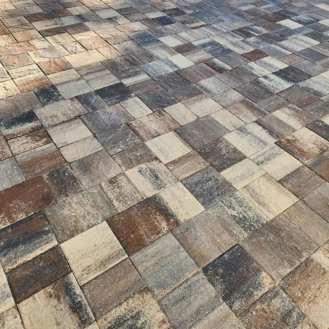 A close-up of a patio surface featuring multi-colored, textured stone pavers in shades of beige, brown, grey, and charcoal.