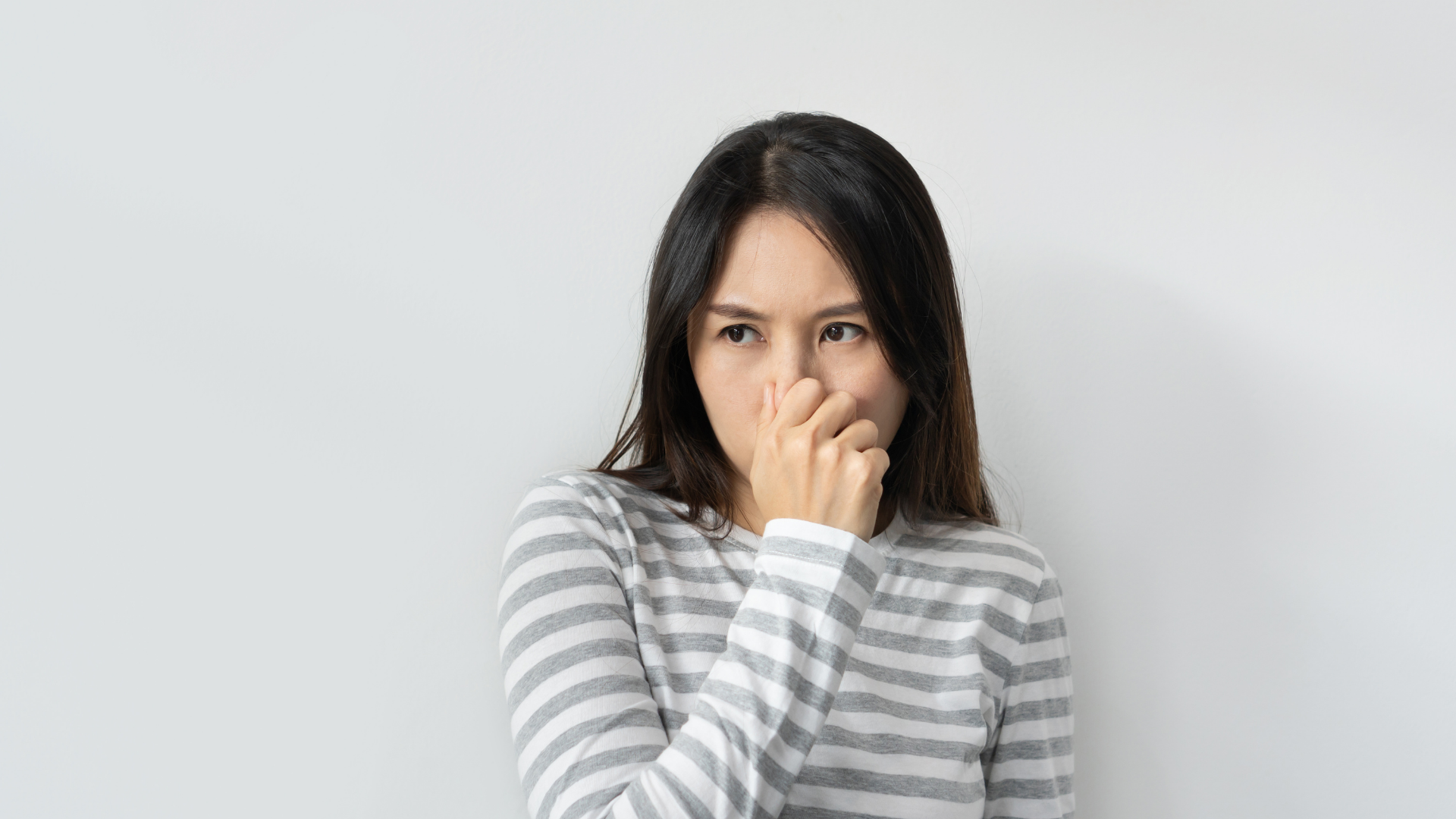 Woman pinching her nose, reacting to a bad smell, with a concerned expression, against a white background.