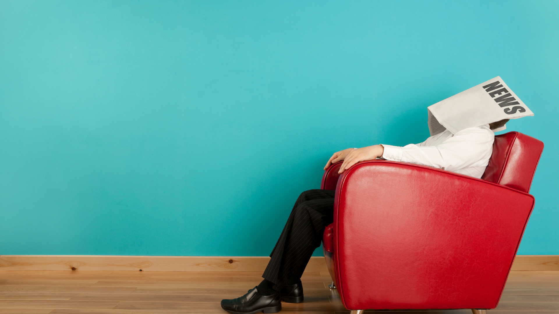 Person slumped in a red armchair with newspaper over head against a teal wall.