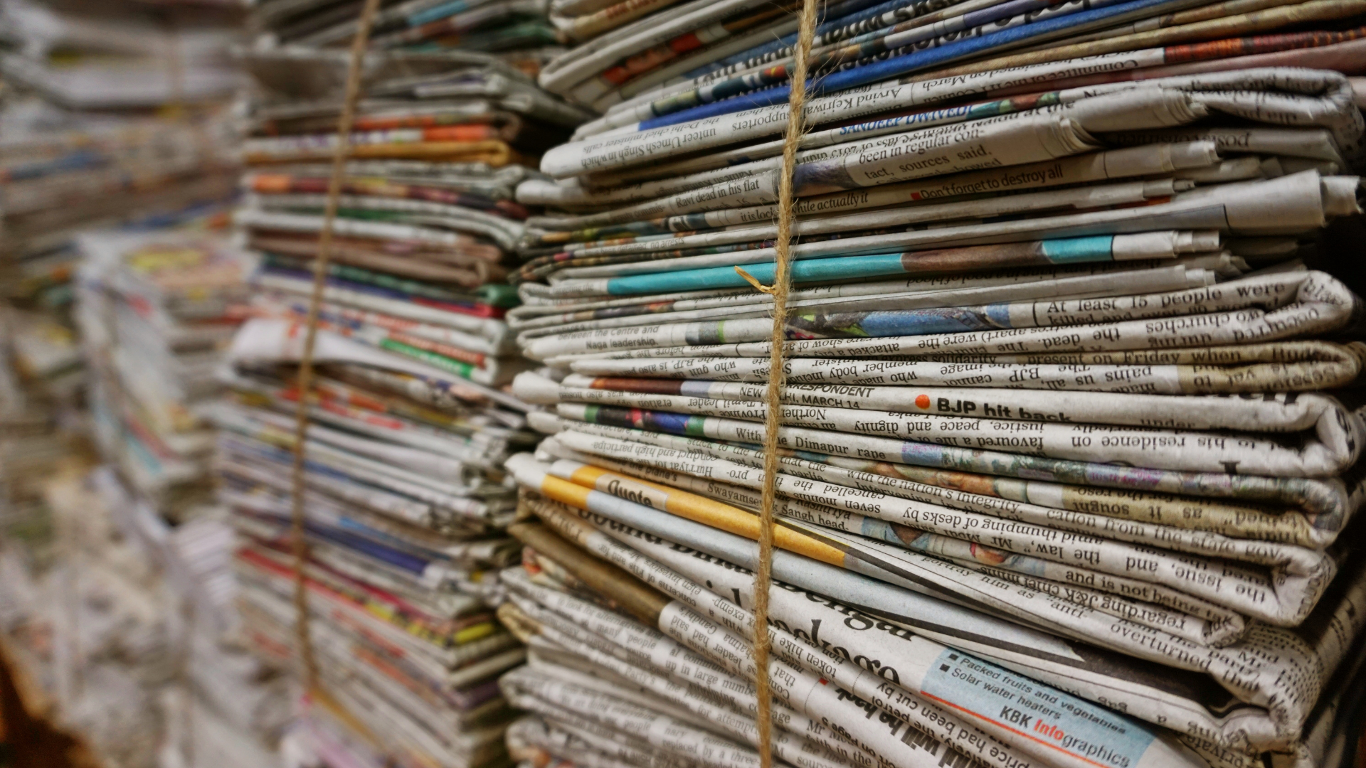 A tall, thick stack of old newspapers tied together with thin twine.