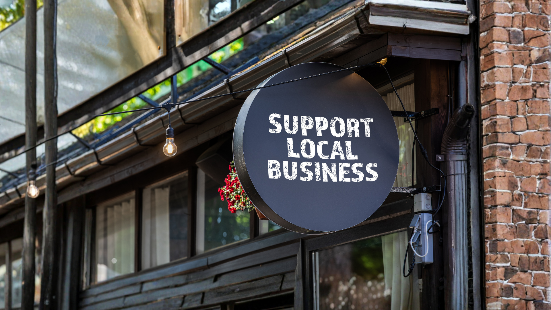 Round black sign reading “SUPPORT LOCAL BUSINESS” on a brick storefront exterior