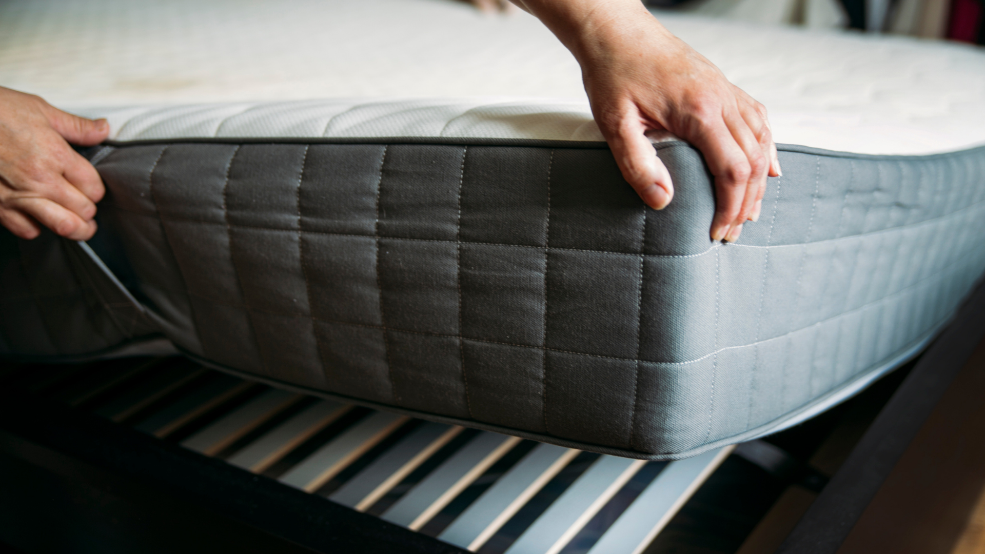 Hands adjusting a gray mattress on a bed frame