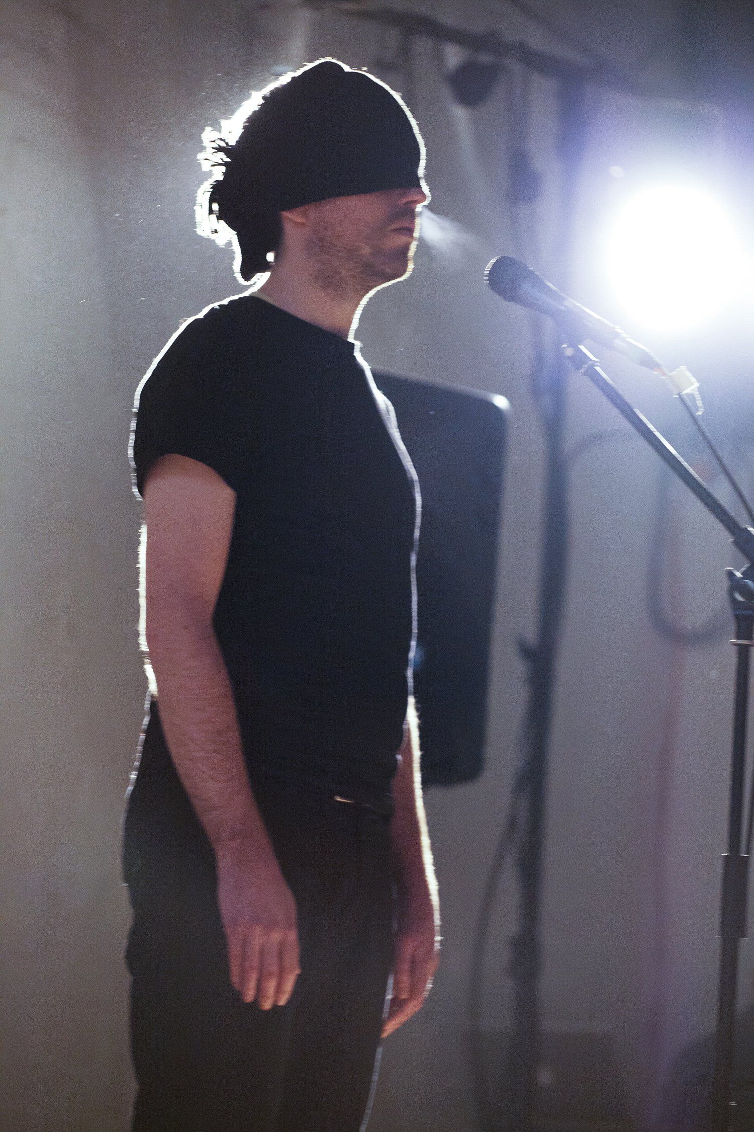 A man in a black shirt is standing in front of a microphone.