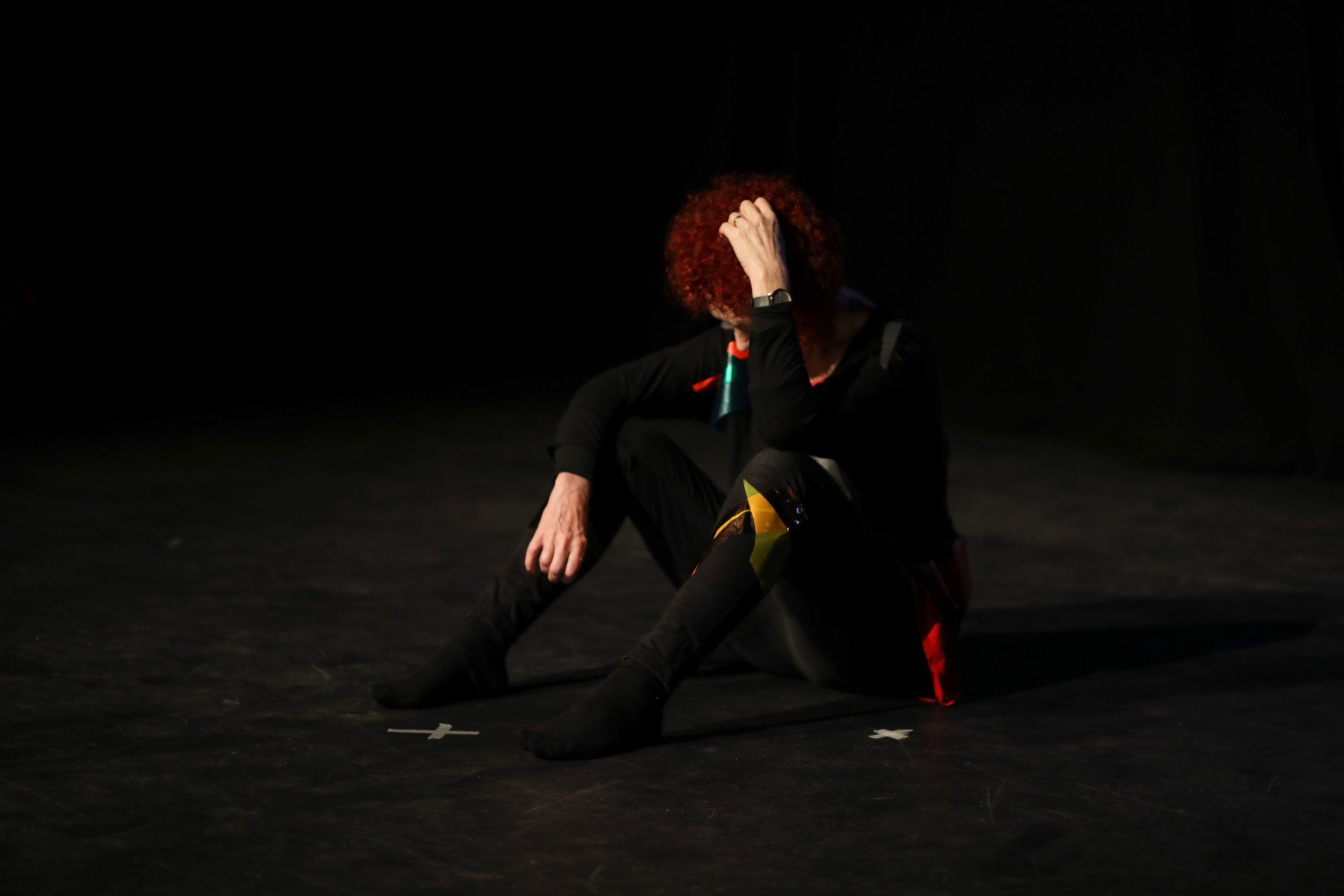 A woman with red hair is sitting on the floor with her head in her hands.