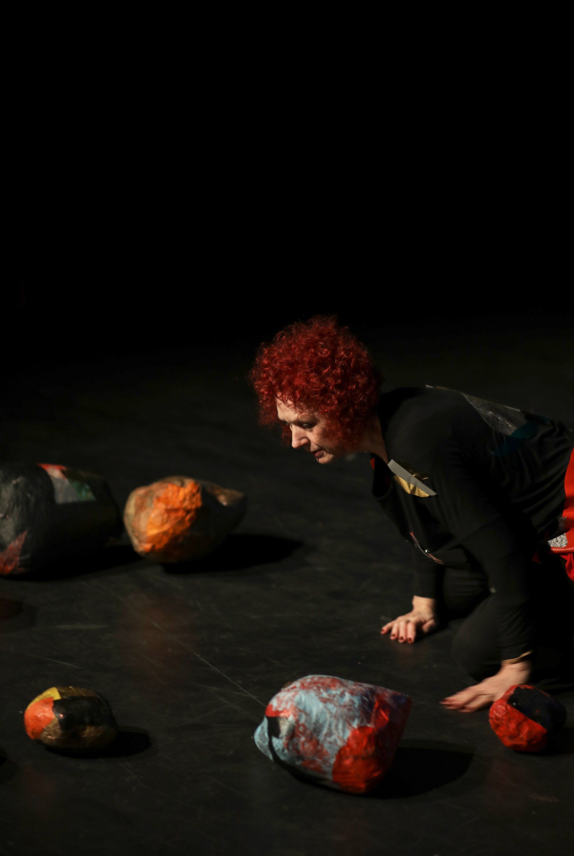 A woman with red hair is crawling on the floor next to a pile of rocks.