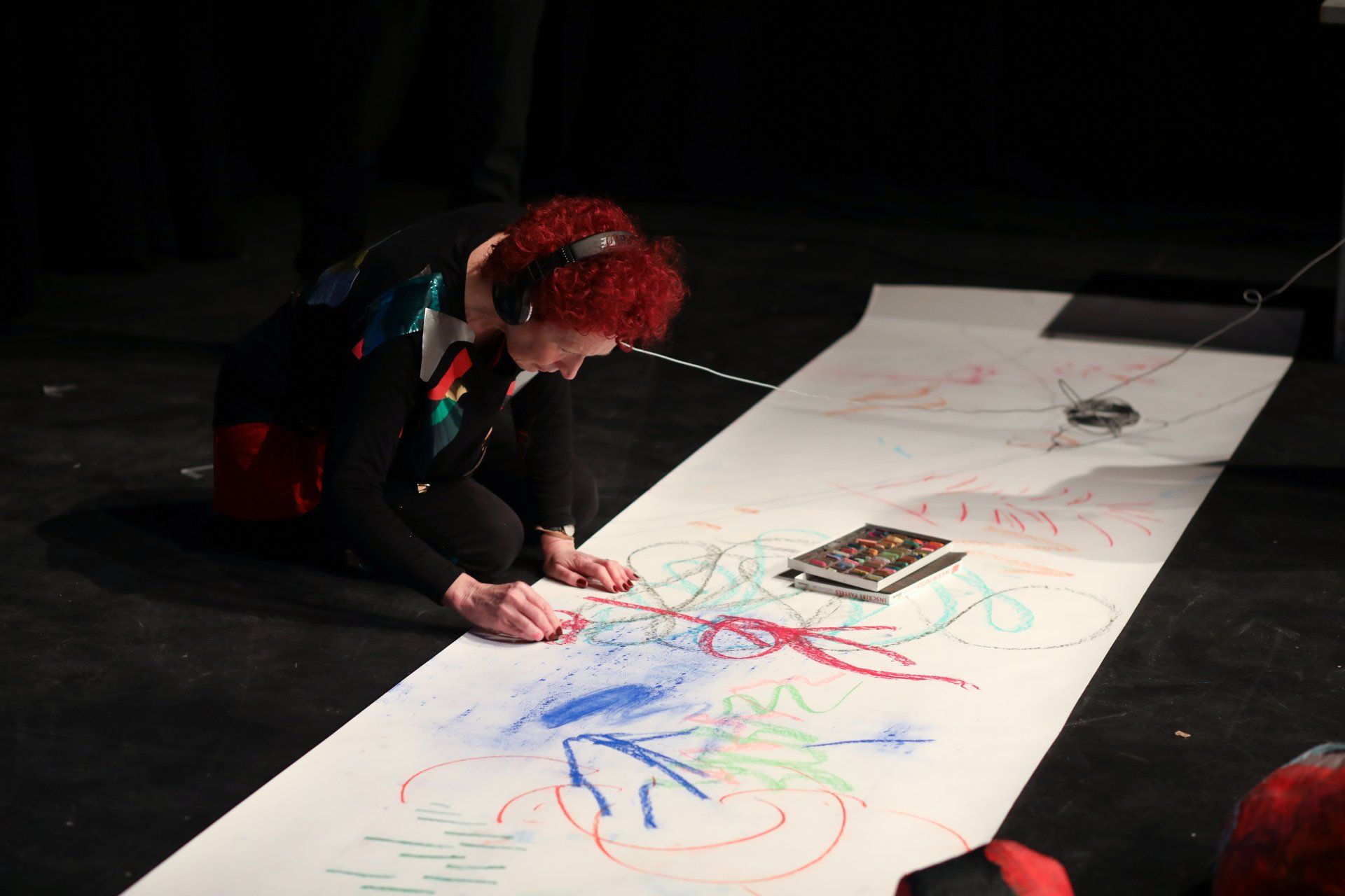 A woman with red hair is drawing on a large piece of paper