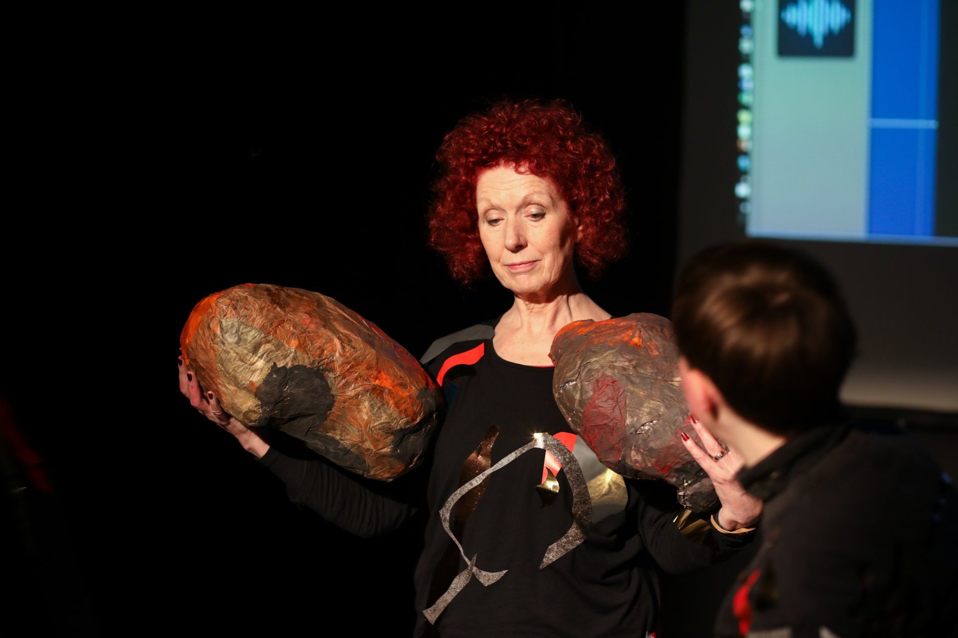 A woman with red hair is holding two large rocks in her hands.