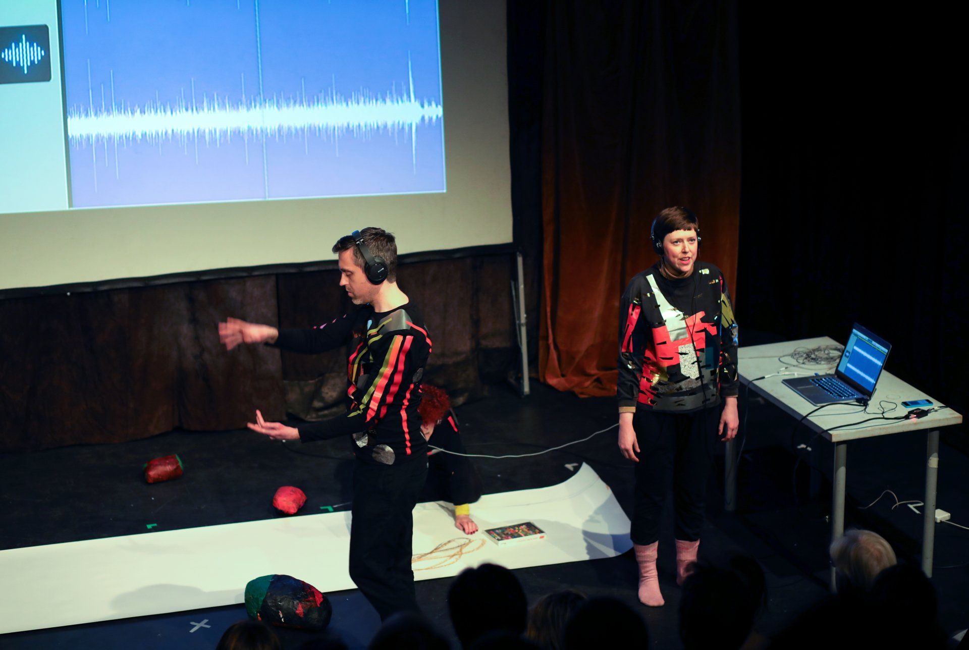 A man and a woman are standing on a stage in front of a projector screen.