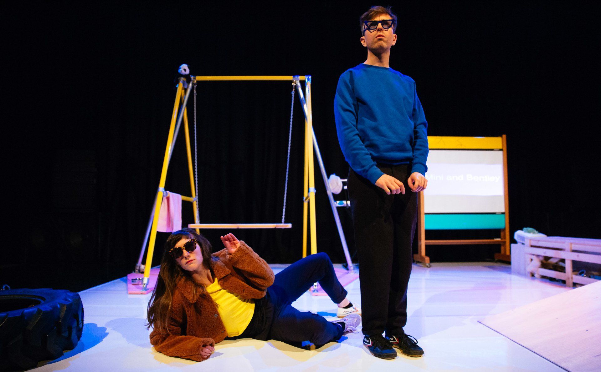 A man and a woman are standing on a stage in front of a swing set.