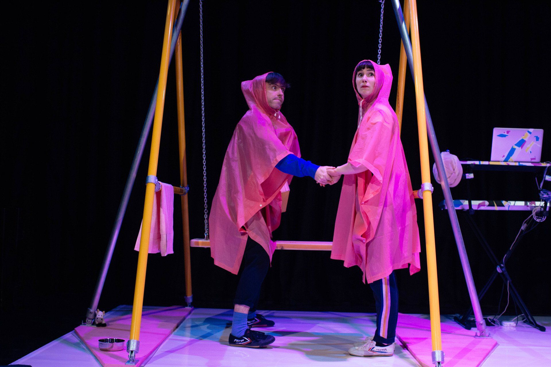 Two people in pink ponchos are shaking hands on a swing.