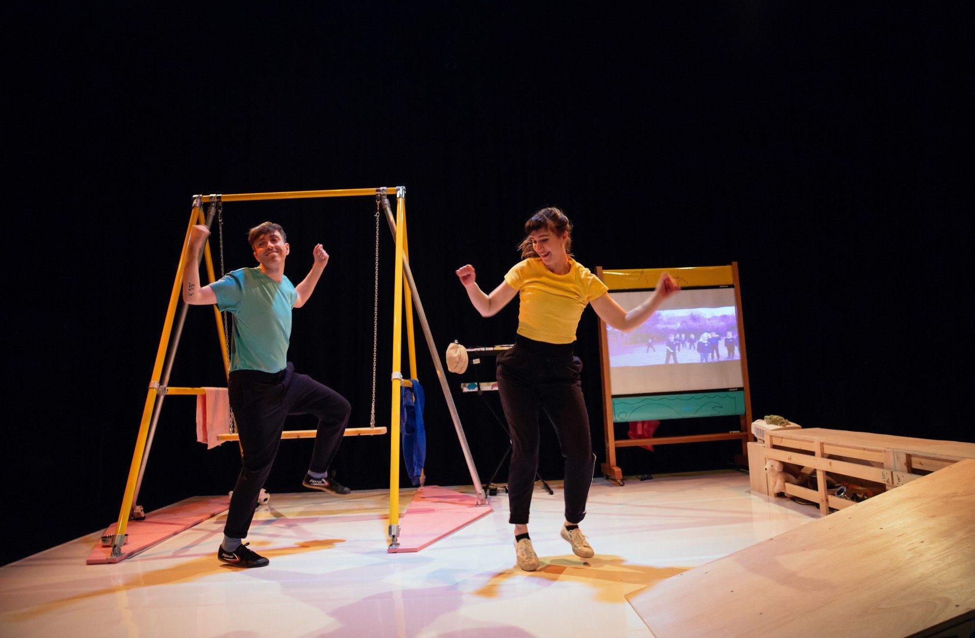 A man and a woman are dancing on a swing set on a stage.