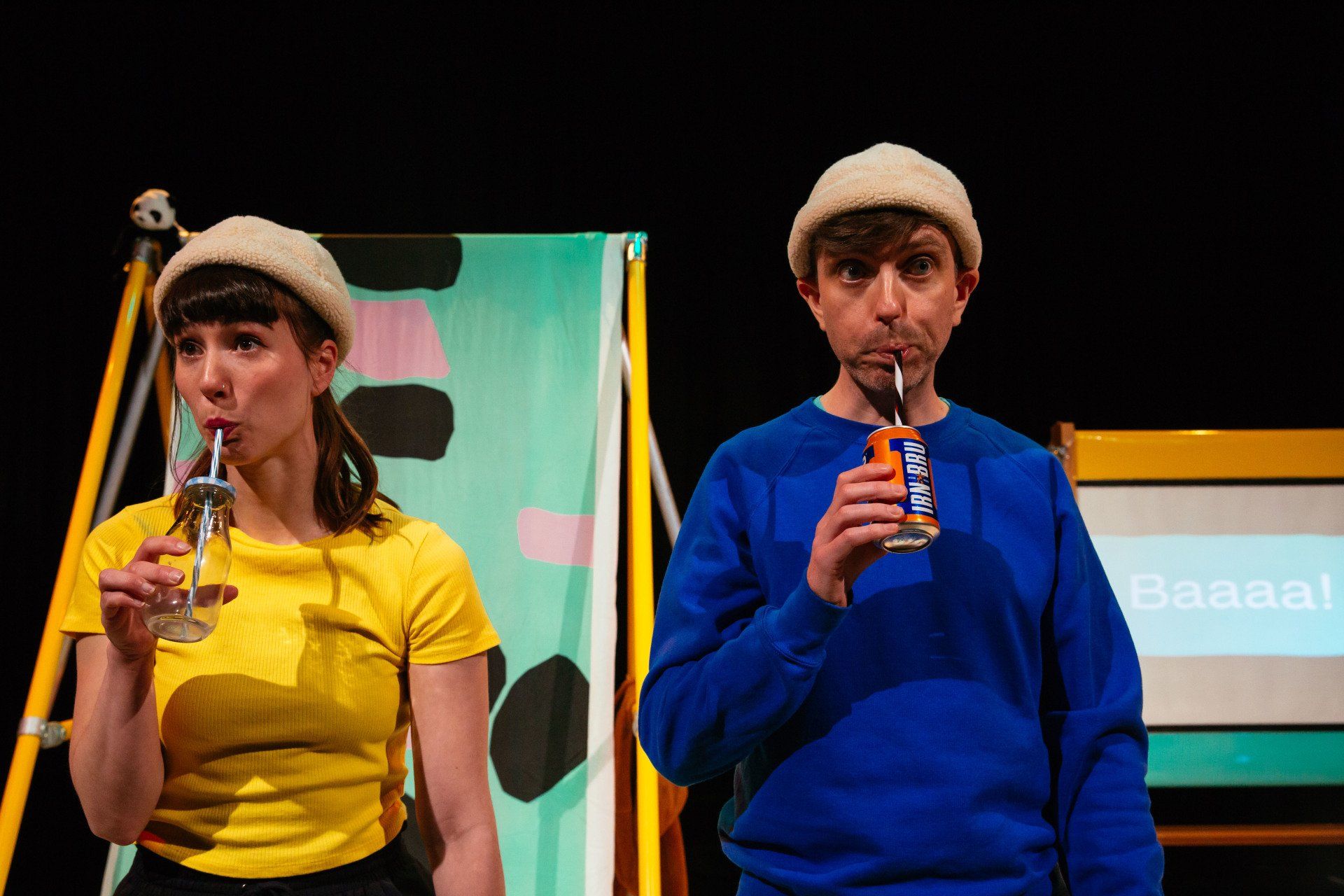 A man and a woman are drinking through straws on a stage.