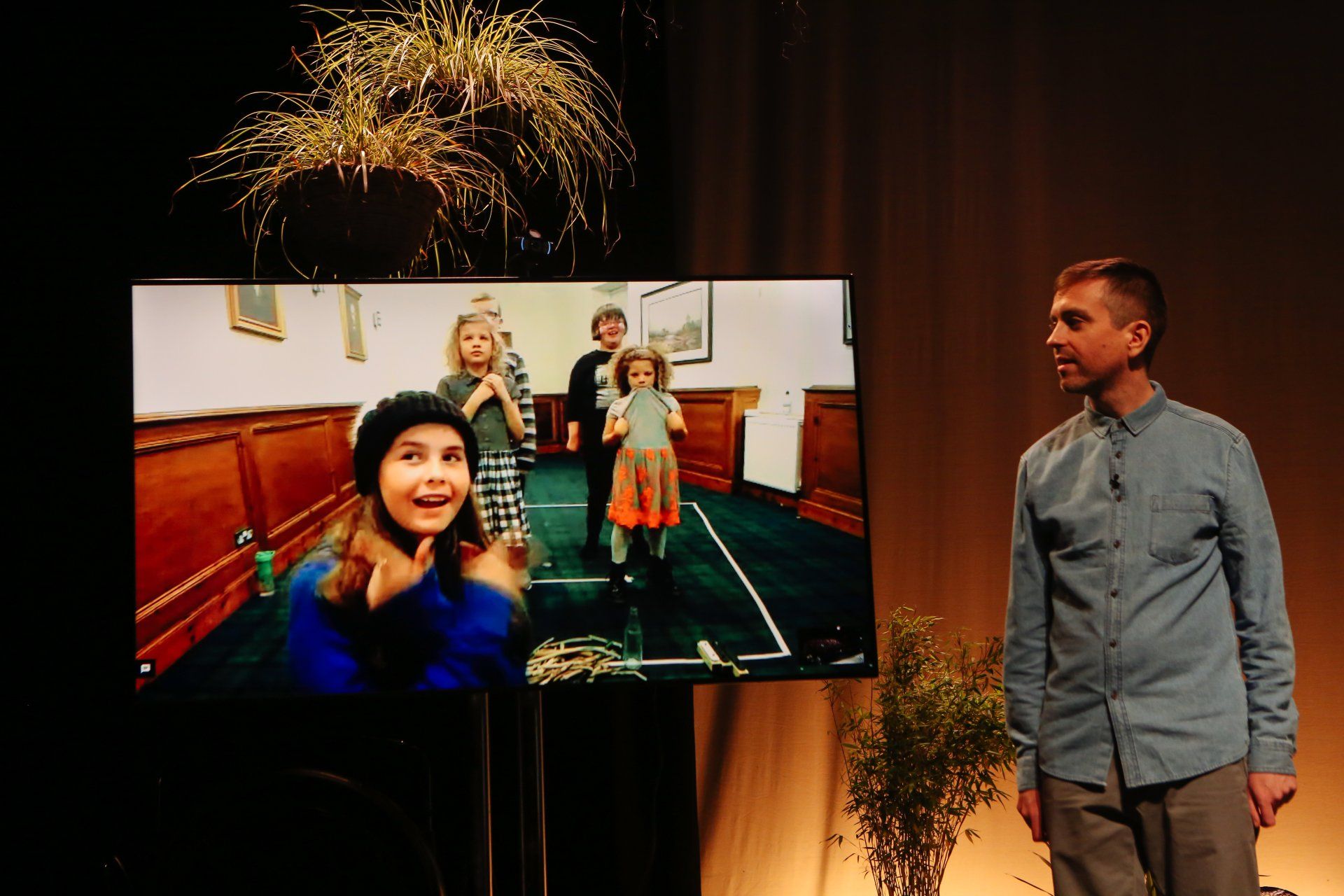 A man is standing in front of a large screen with a picture of children on it.