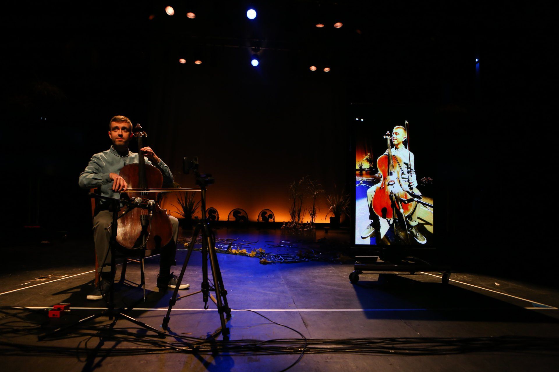 A man is playing a cello on a stage in front of a screen.