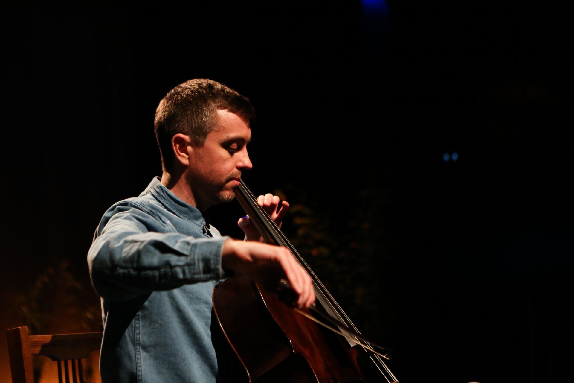 A man is playing a cello in a dark room.