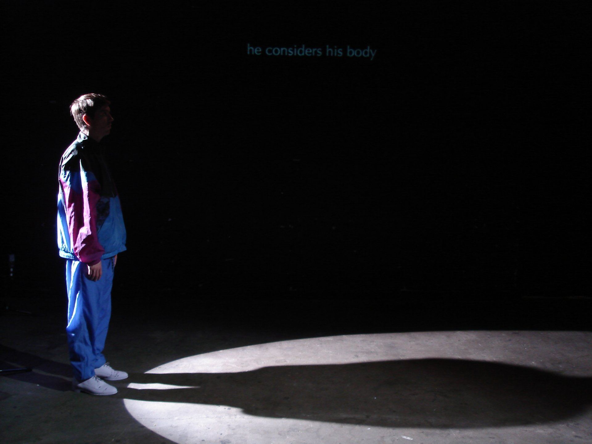 A person standing in a dark room with a sign that says he considers his body